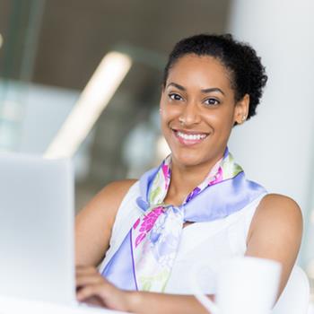 Woman in front of laptop, smiling at camera
