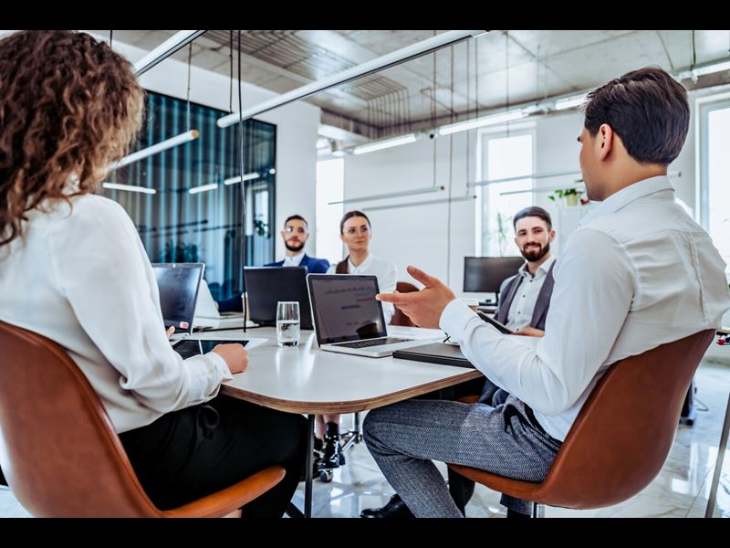 Shot of business young people sitting in chairs at the table with computer and laptop