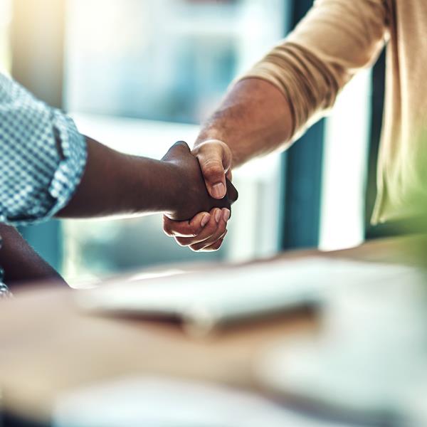 Two people shaking hands while sitting at table