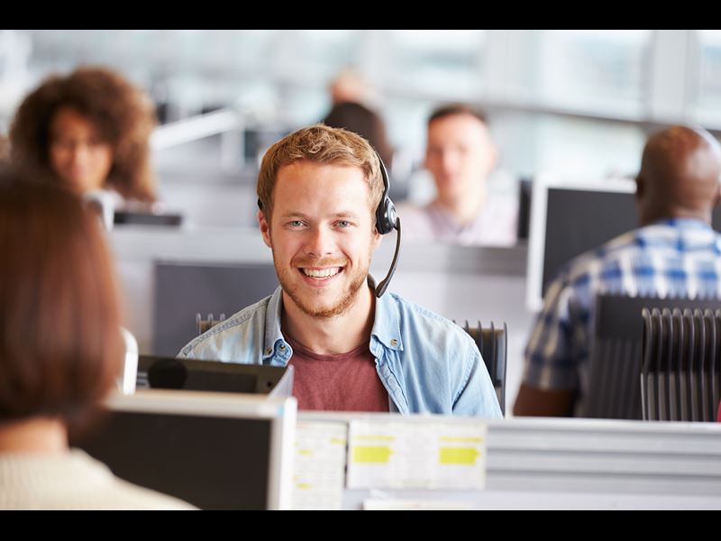 Male Employee With Headset Smiling While In A Call Center Setting