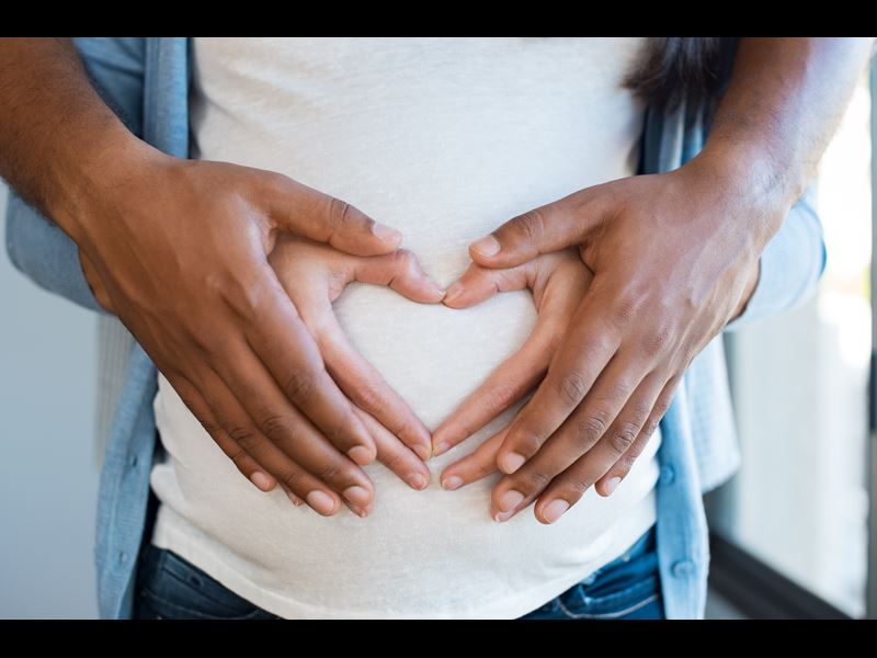Assurant Blog Image: Couple holding hands in heart of woman's pregnant belly