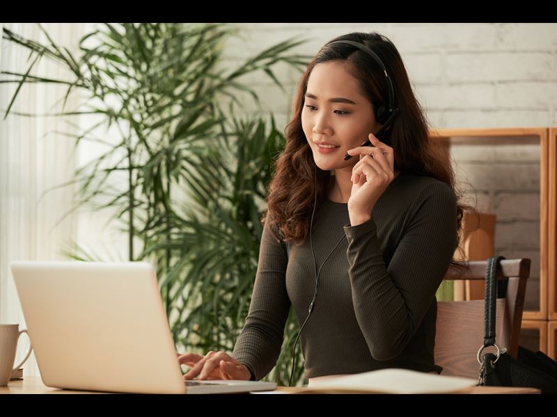 Woman sitting in front of laptop and talking on headset