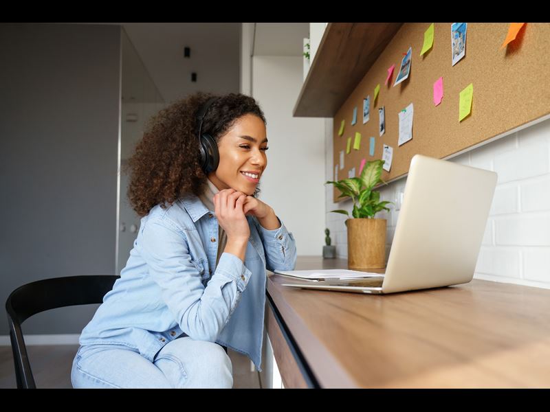 Woman working from home with headset on, smiling at laptop