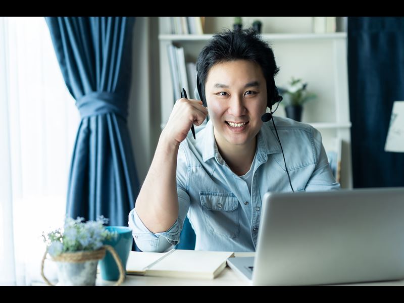 Man wearing headset, smiling at camera with laptop in front of him