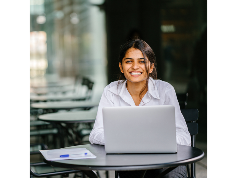 Smiling woman sitting at cafe table in front of laptop