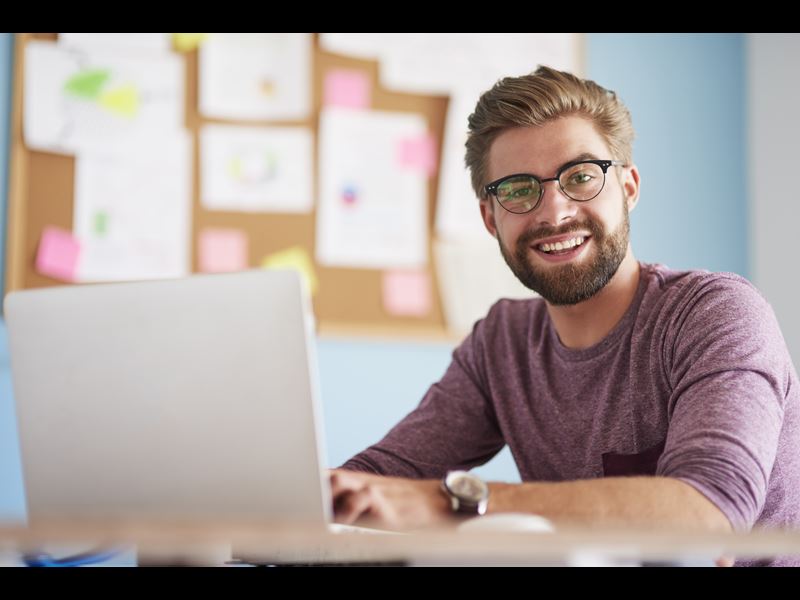 Man sitting in front of laptop, smiling at camera