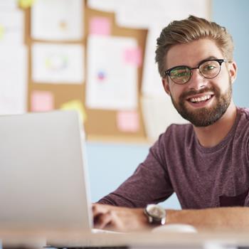 Man sitting in front of laptop, smiling at camera