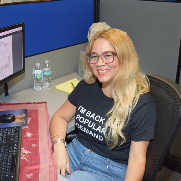 Assurant employee smiling at office desk with shirt that reads "I'm Back by Popular Demand"