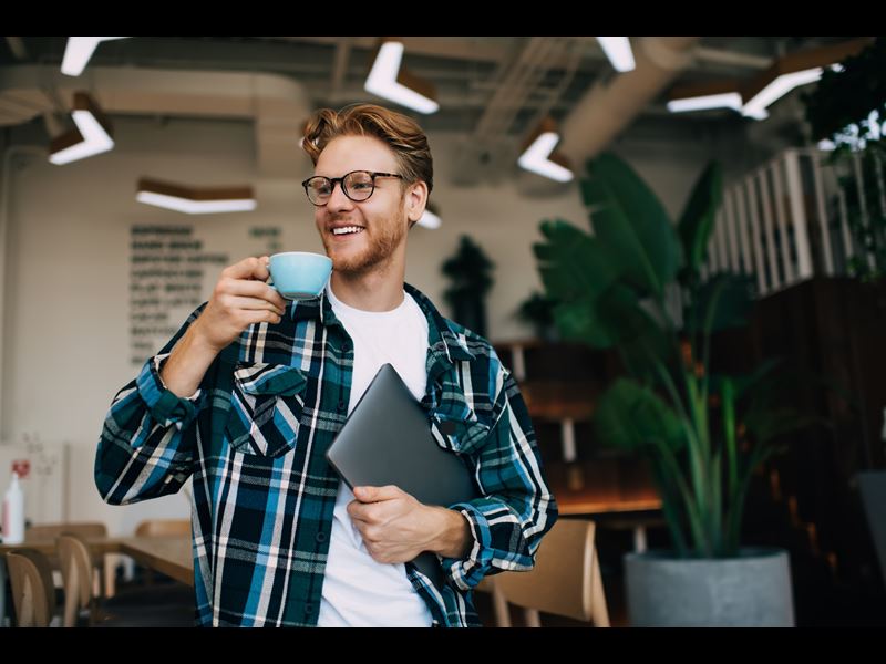 Man Smiling Sipping Tea And Holding Laptop