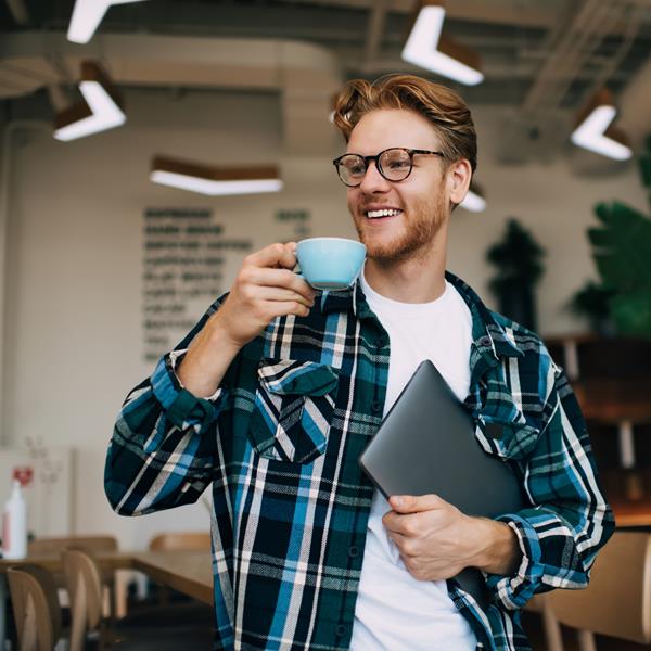 Man Smiling Sipping Tea And Holding Laptop