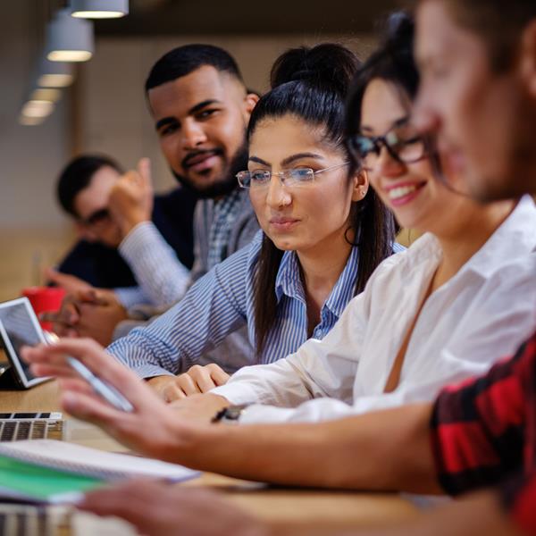 Five people working at desk, looking over at each other's devices