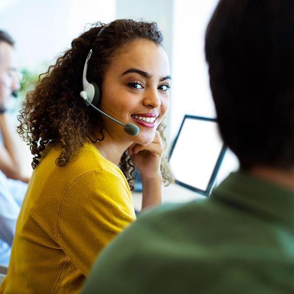 Three people wearing headsets and working from their desks with the woman in the middle smiling at the camera