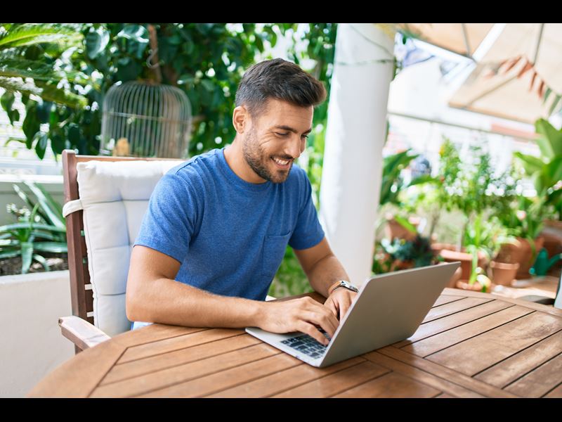 Man working from outdoor location, smiling at laptop